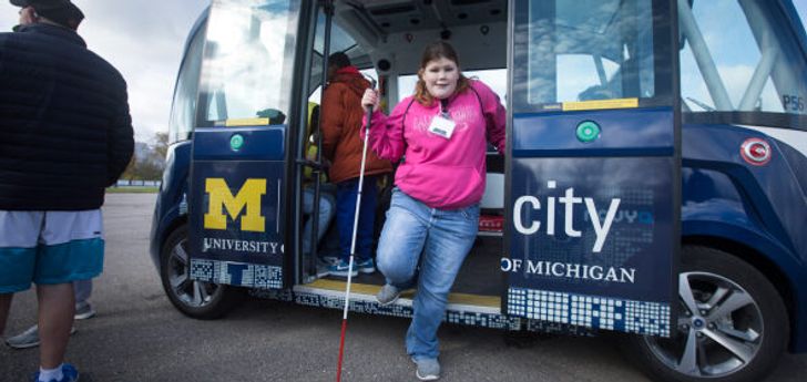 A person with a white cane stepping out of an MCity vehicle